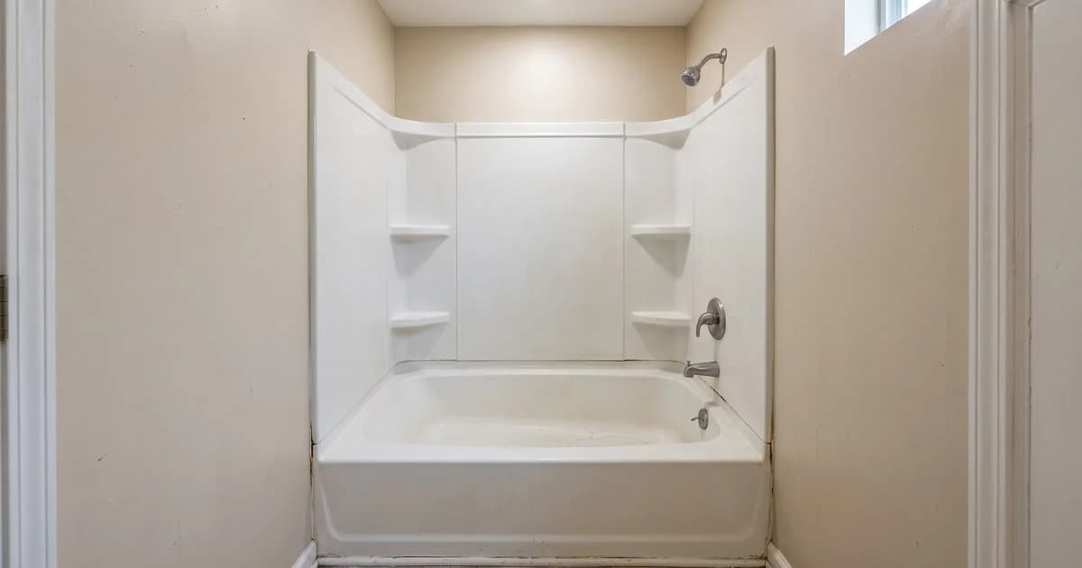 An ageing fiberglass tub-shower surround with hairline cracks in the tub floor and a darkened caulk line.
