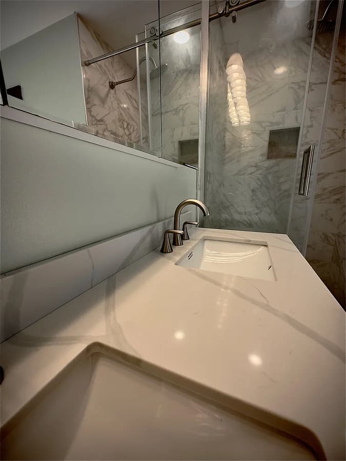 Undermount sink and brushed-nickel faucet on the vanity top, with the tiled shower beyond the glass.