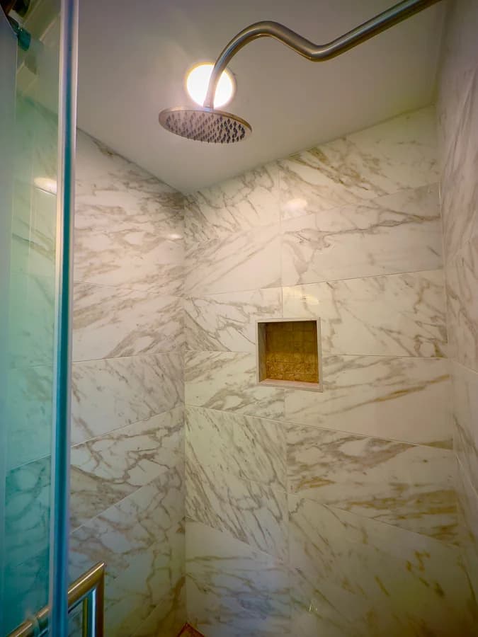 Looking up inside the shower at the round rain head and the recessed niche set into veined wall tile.