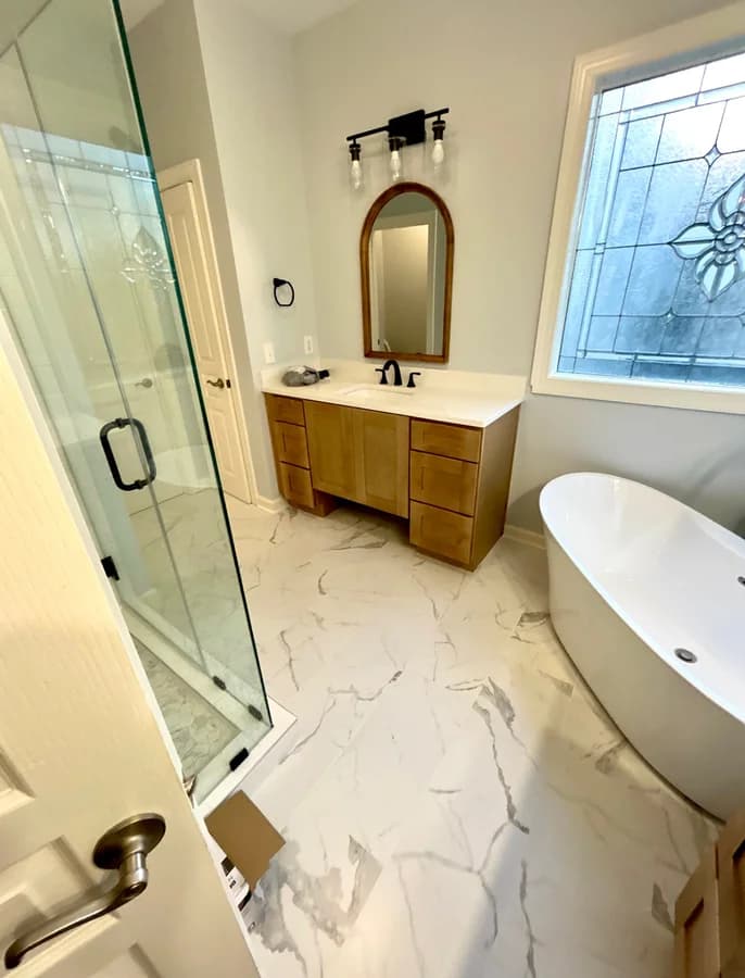 Wood vanity with an arched mirror and black fixtures, the glass shower at left and the tub at right.