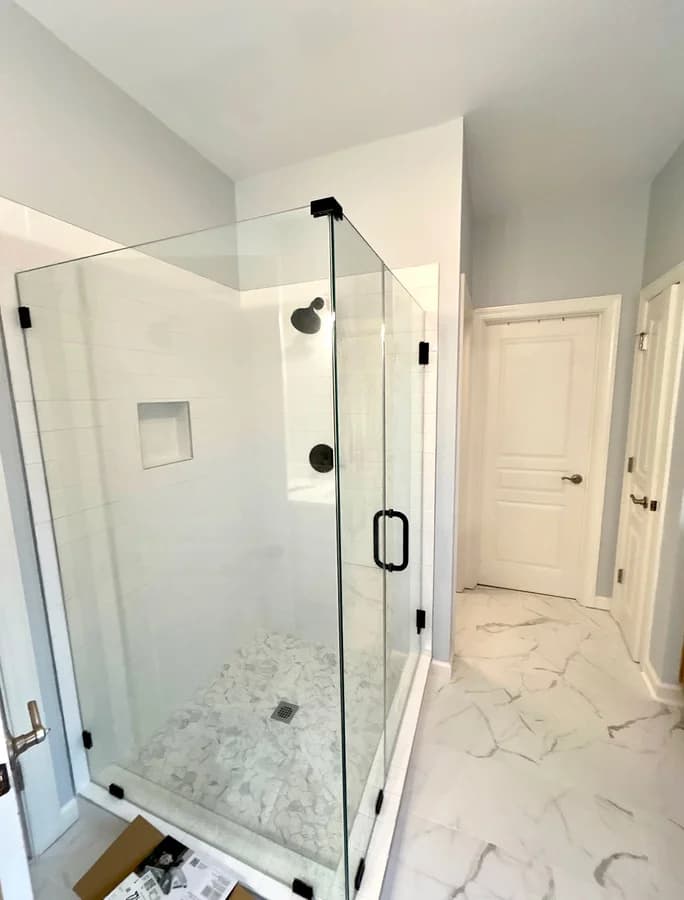 Corner glass shower with white wall tile, a recessed niche and a pebble-look mosaic floor.