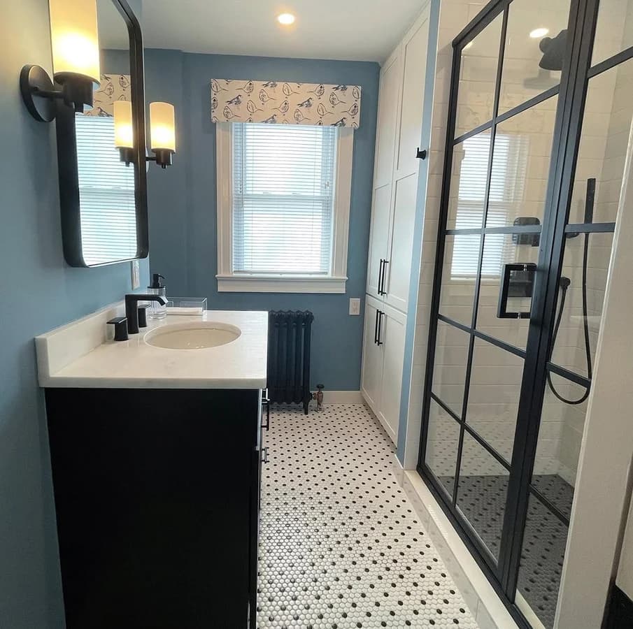 Narrow bathroom with a black grid shower screen, penny-round floor tile and a cast-iron radiator.
