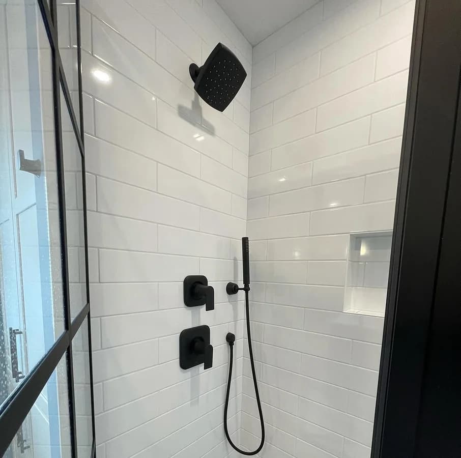 White subway tile shower with matte black fixtures, a handheld on its rail and a recessed niche.