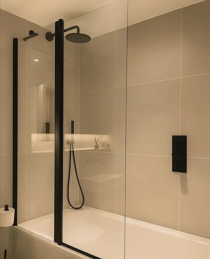 Bath with a black-framed screen, a round rain head and a handheld on the large-format wall tile.