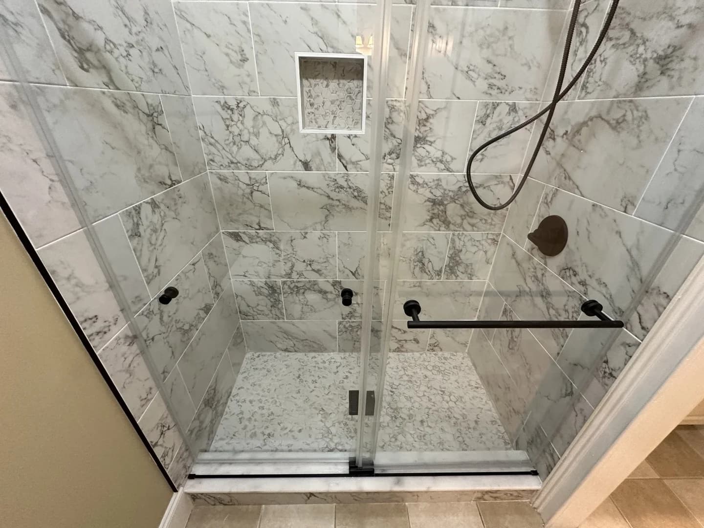 Wide bathroom view showing the completed enclosed shower with glass doors and matte black hardware.
