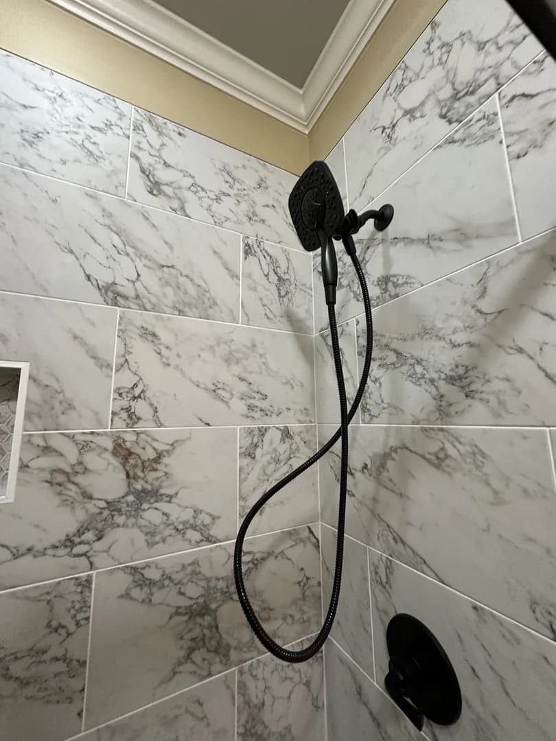 Matte black handheld shower fixture installed against large-format marble-look wall tile.