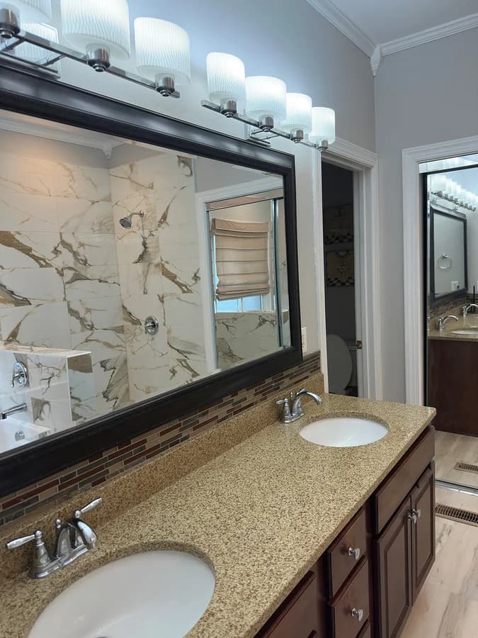 Double vanity with a speckled granite top, framed mirror and glass mosaic accent strip below it.