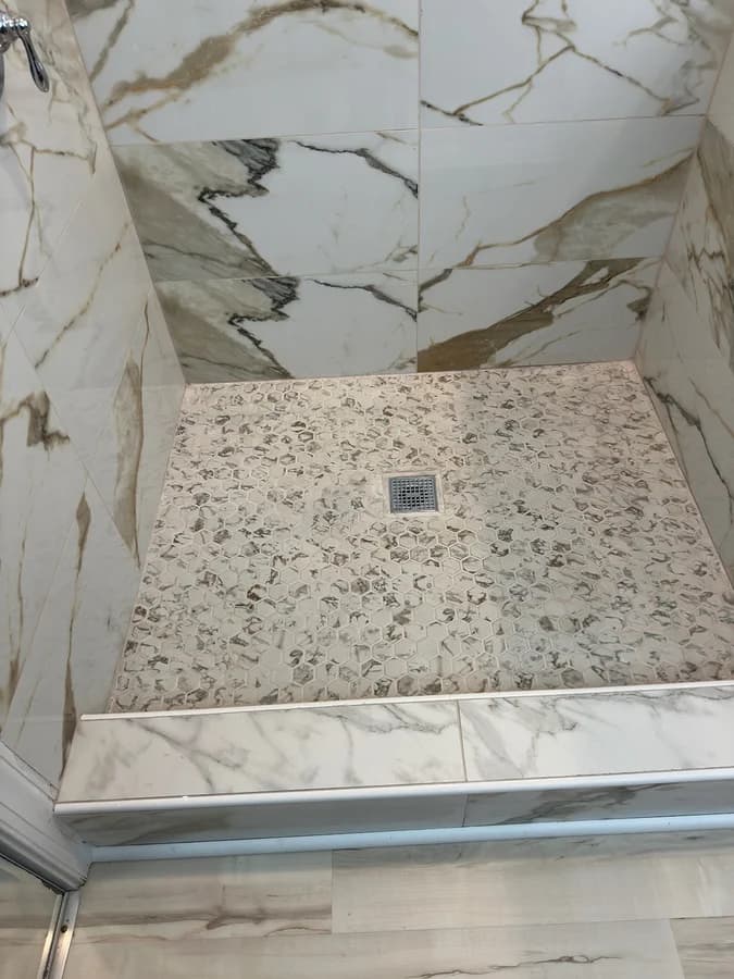 Hexagon mosaic shower floor sloped to a square chrome drain, framed by a tiled curb.