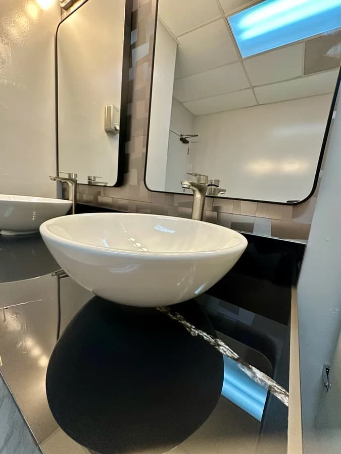 Vessel basin against the geometric metallic backsplash, with the black-framed mirror above it.