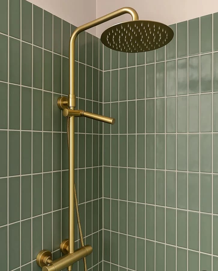 Exposed brass shower column with a round rain head and handheld against green stack-bond tile.