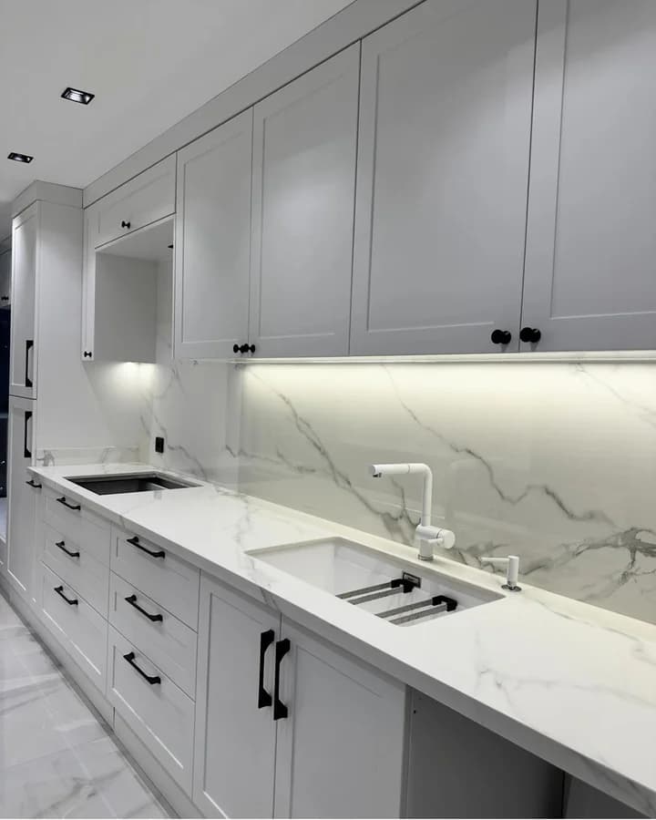 Run of shaker cabinets over a marble-look counter and backsplash, with two undermount sinks.