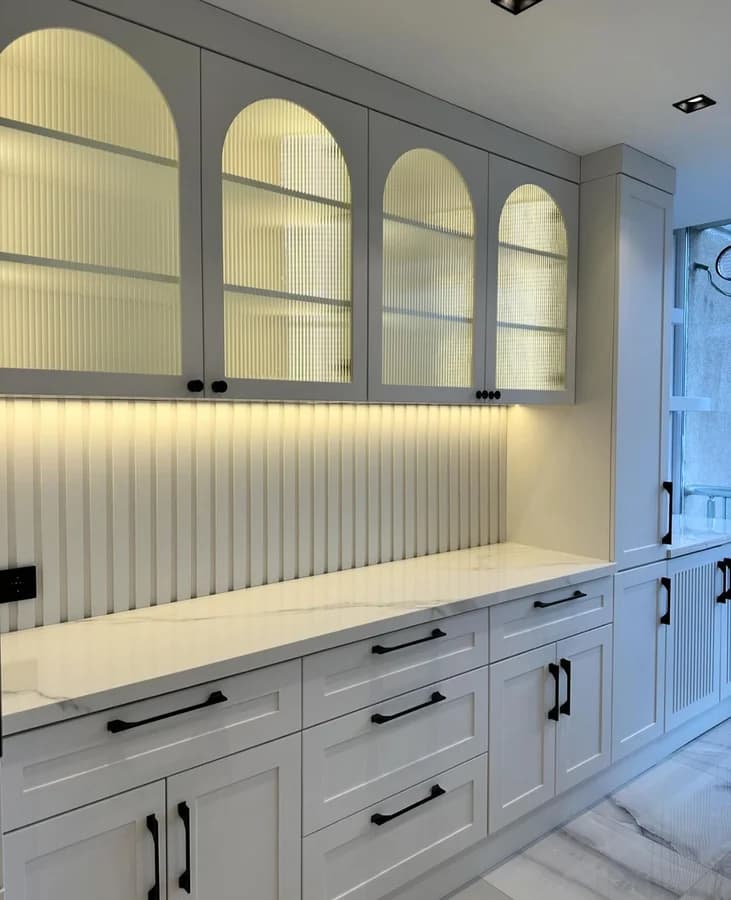 Arched reeded-glass wall cabinets above a fluted backsplash and a marble-look counter.